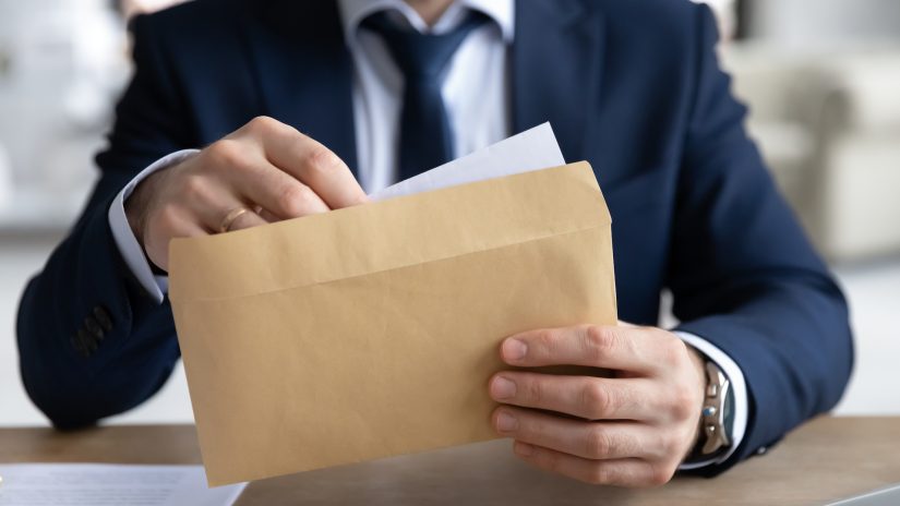 Insurance adjuster in suit pulling settlement demand letter out of envelope. 